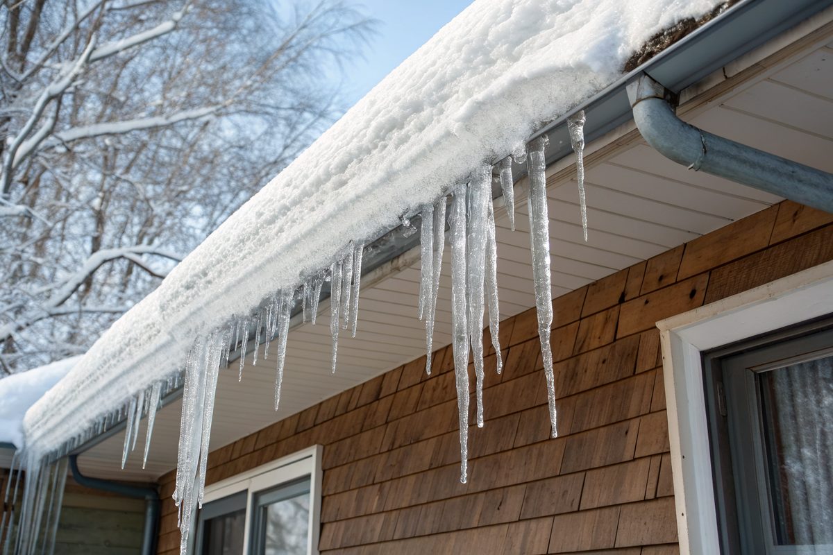 Heavy snow and long icicles hanging from the gutter of a wood-sided house