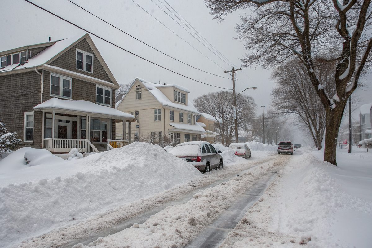 Deep snow banks, buried cars and snow-covered roofs along a street of older two-story houses